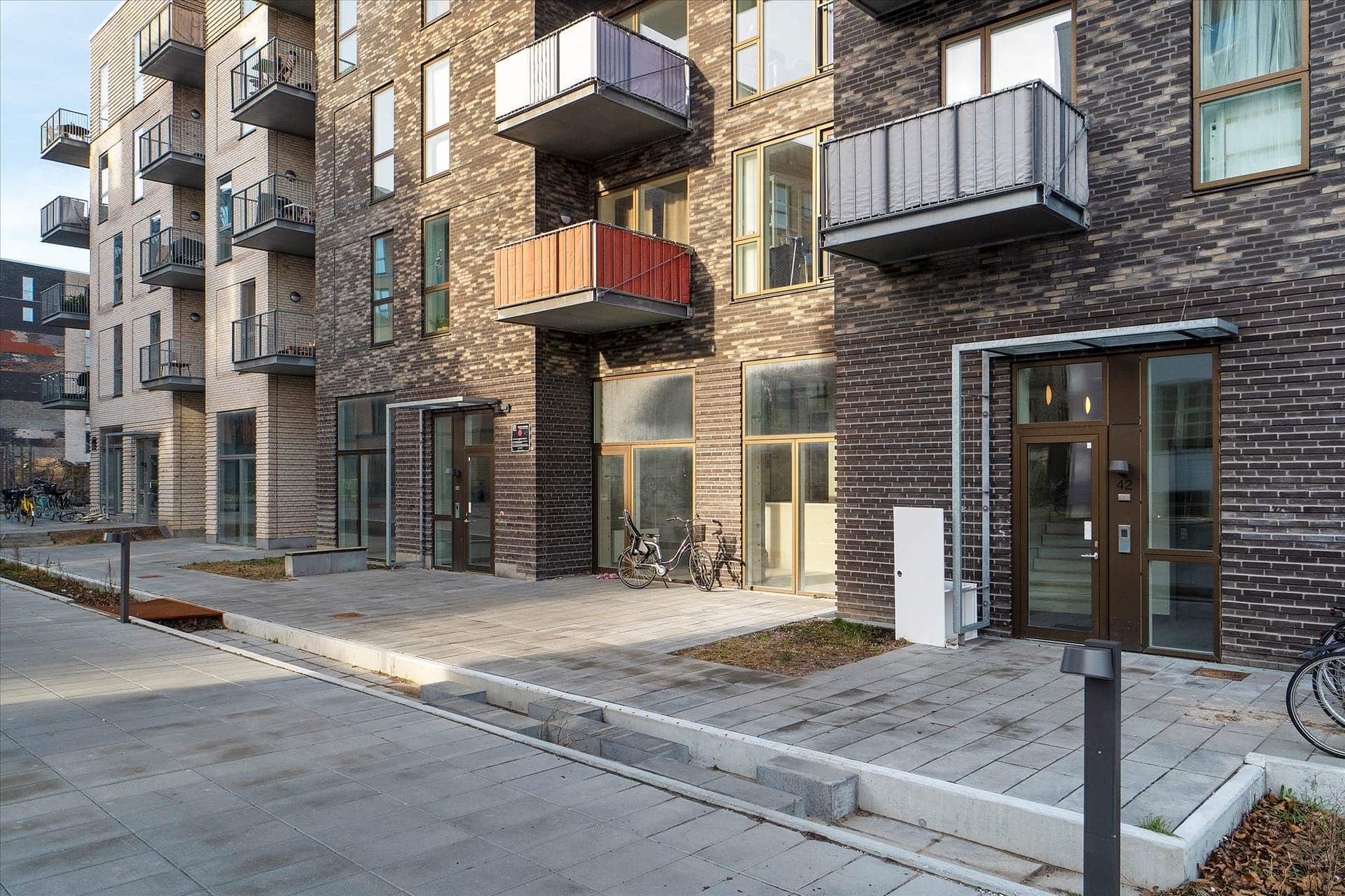 Lejlighedsbygning med terrasser og indgange, hvor en cykel står parkeret og en anden cykel står ved siden af en søjle