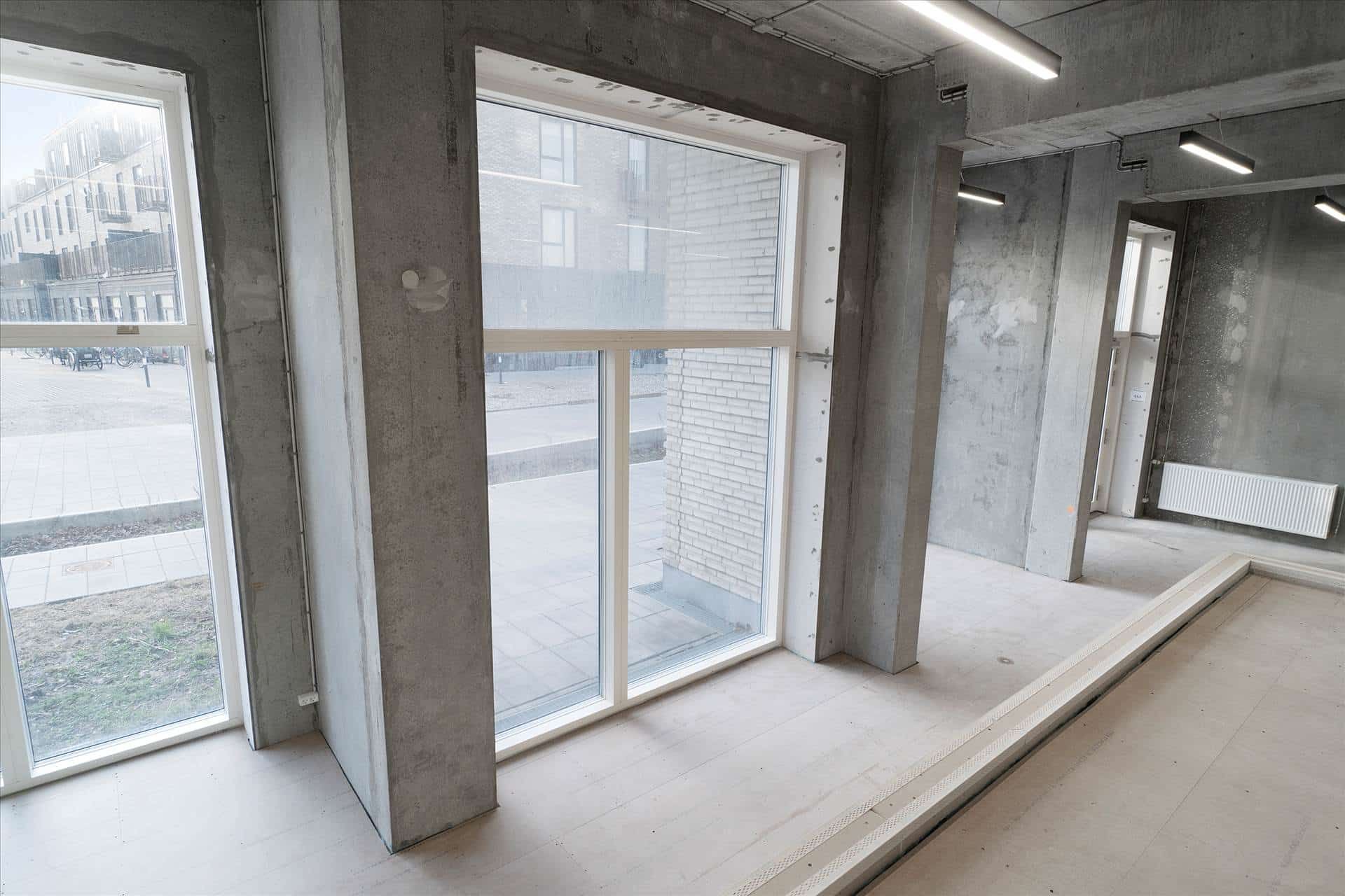 To store vinduer i en renoveret kontorlokal med lyse, glasvægge og hvidgulvet. Bag vinduet er der et tomt parkeringsområde