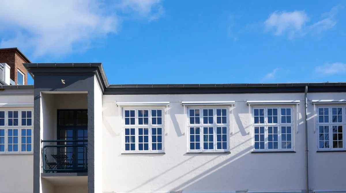 Hvidt nyrenoveret lejlighedshus med røde vinduer og balkoner og røde mursten i baggrunden