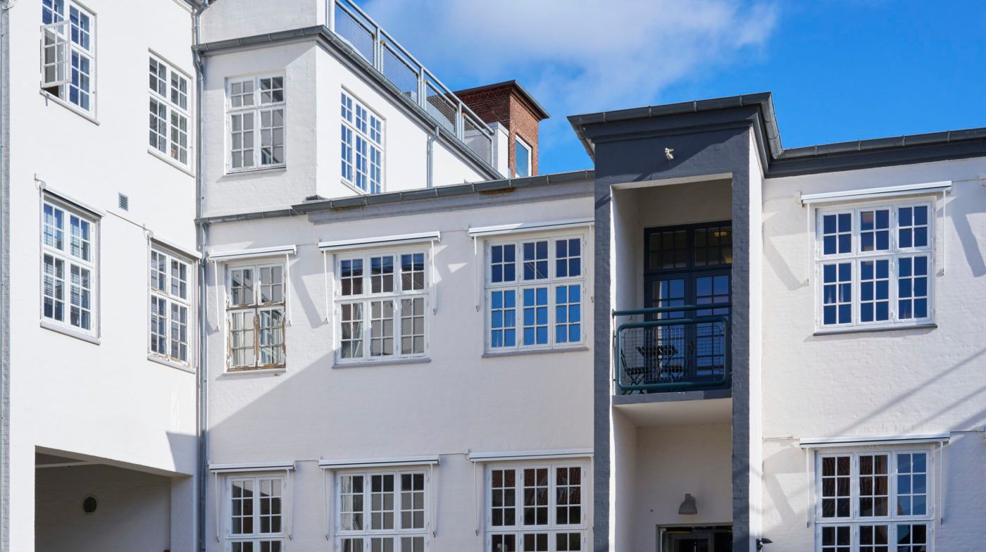 Lejlighed i renoveret hus i Nedergade Kvarter i Odense. Balkon med stol og bord samt søjler med tag på lejlighedsbygning.