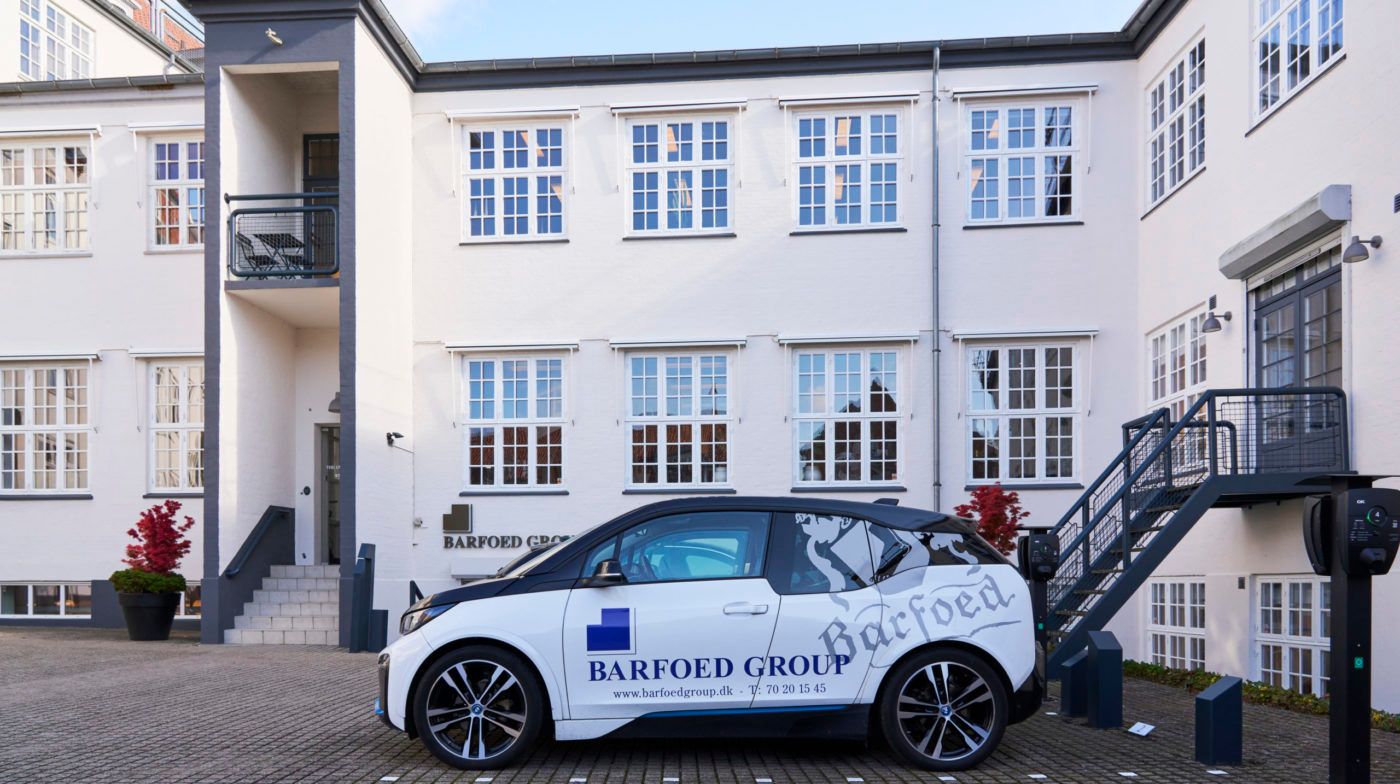 En elektrisk BMW i8 parkeret foran Barfoed Group hovedkvarter i Odense, med Barfoed Group logoet og sloganet på siden