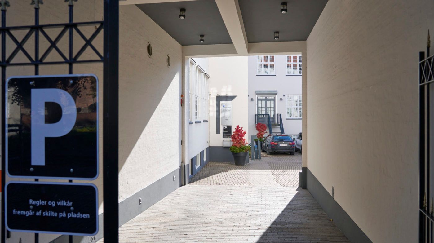 Indkørslen til parkeringspladsen, med røde planter i potter og parkerede biler, der venter på deres ejere