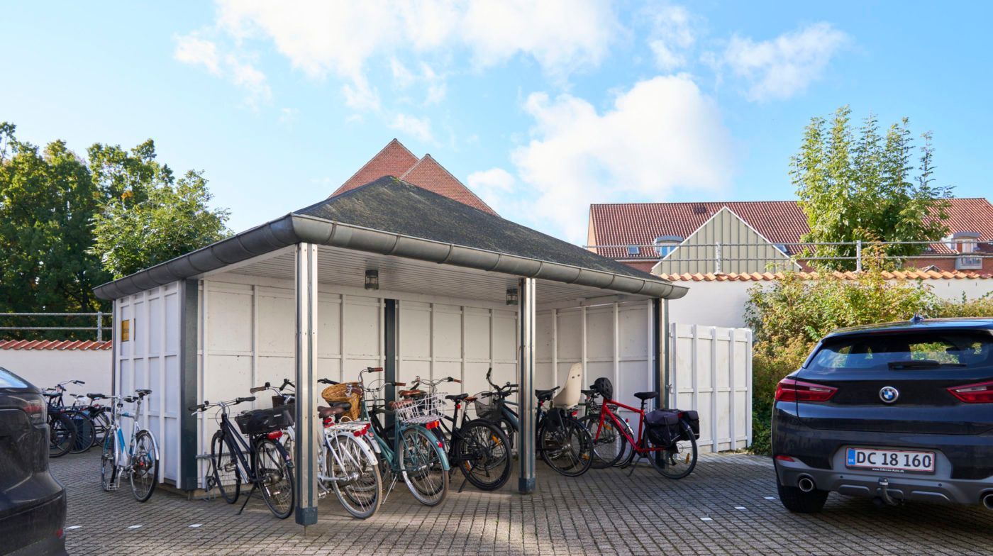 Garage med fire cykler og to biler parkeret i baggrunden og et BMW køretøj står parkeret foran garagen