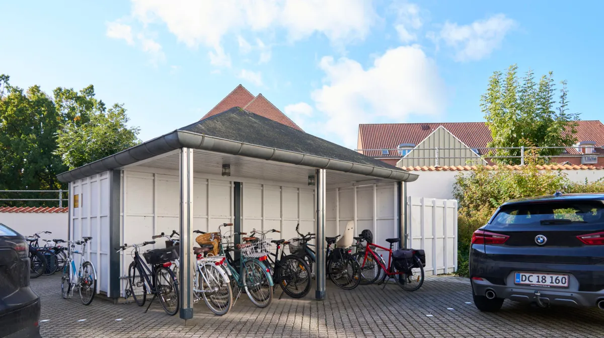 Garage med fire cykler og to biler parkeret i baggrunden og et BMW køretøj står parkeret foran garagen