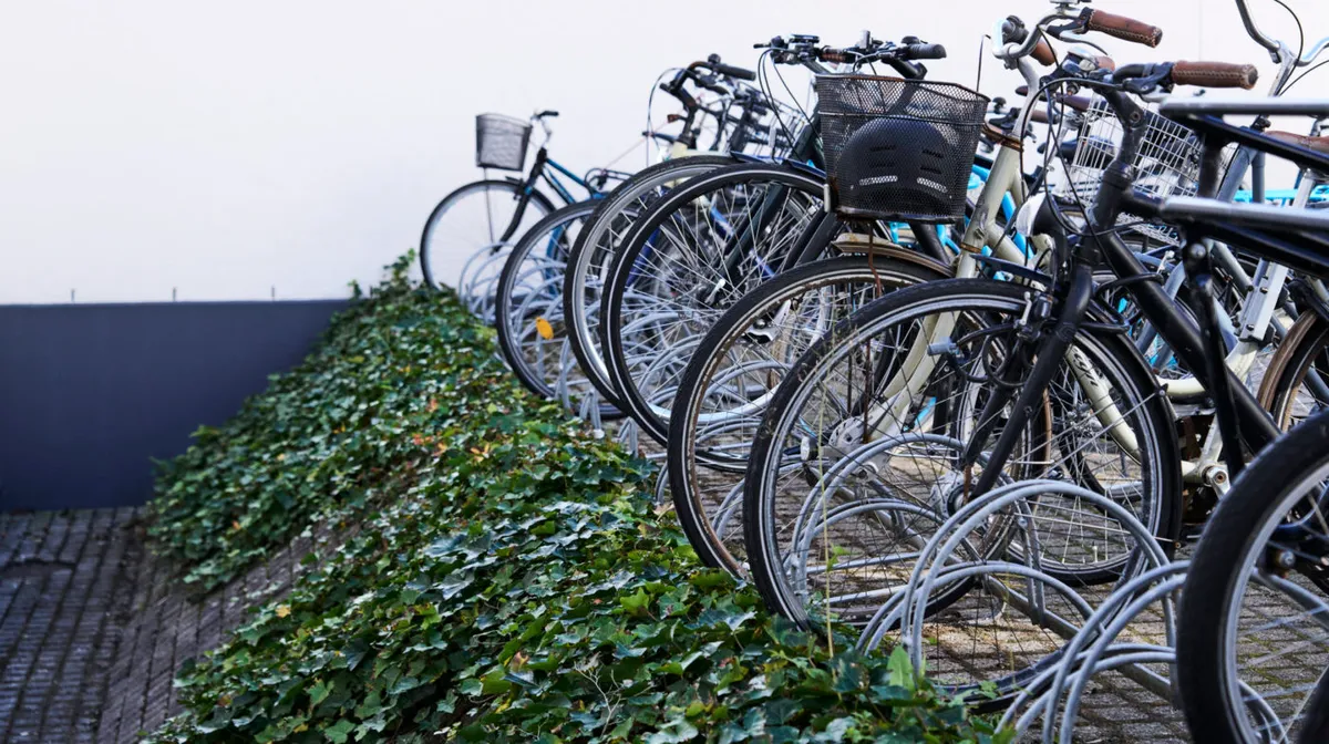 Adgangsvej til parkeringsplads med række med stillestående cykler, hvoraf en har hjelme og kurve i bagagebæreren