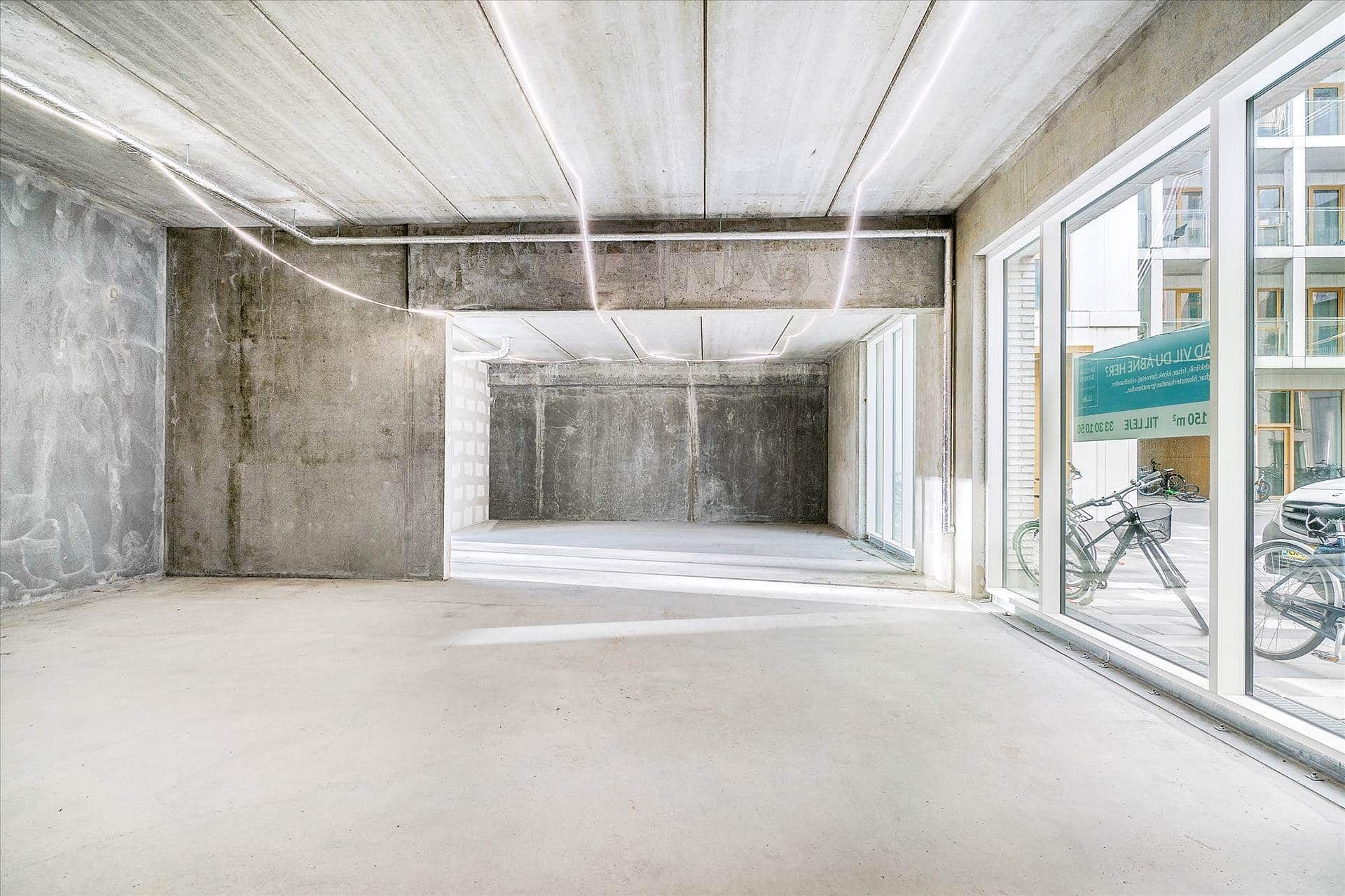 Store glasvinduer med skilte og refleksioner af cykler og biler i en moderne og minimalistisk bygning