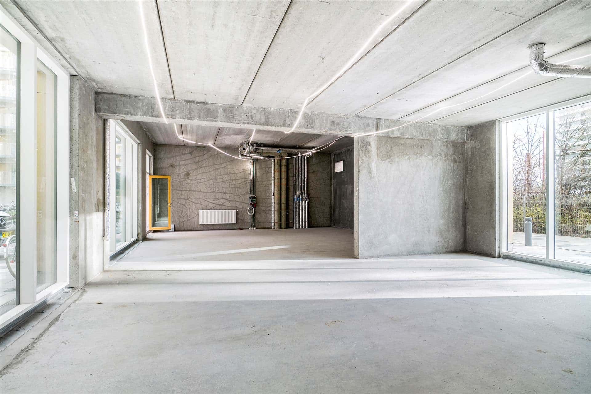 En stor, lys og tom bygningsindgang med glasdøre og vinduer, belyst med hvide lysbånd og en gul dør i midten