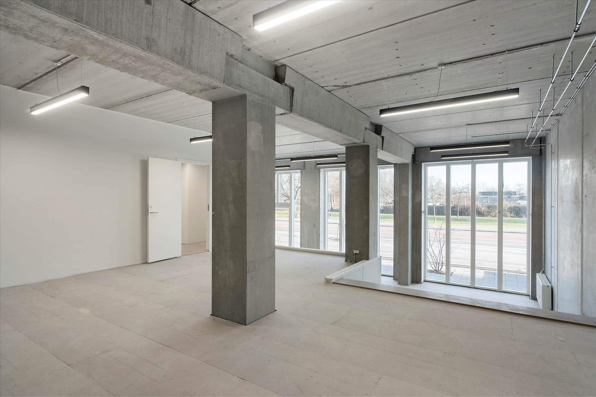 Moderne kontor med højloft og lyseruder samt hvide vægge og cementgulv, flere lysekroner og trægulv i visse dele