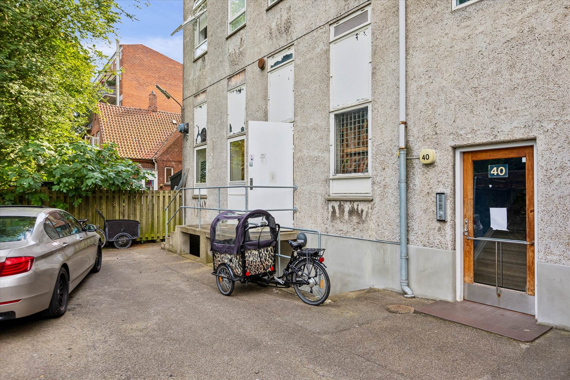 En gul bil parkeret i en gade, et cykeltræk med leopardprint og et rødt hus med rødt tag og terrasse.