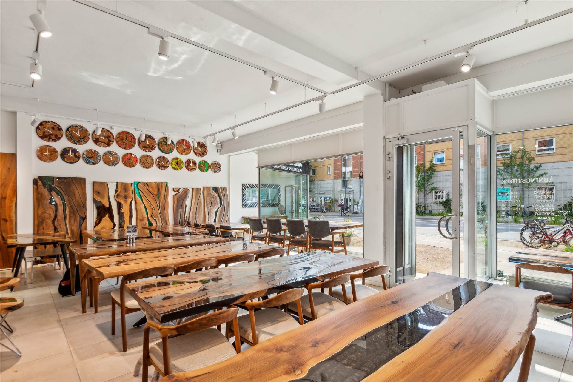 En stor indretning med lyse lofter, store vinduer og lange træborde med møbler i en bygning med møbler og ure på væggen