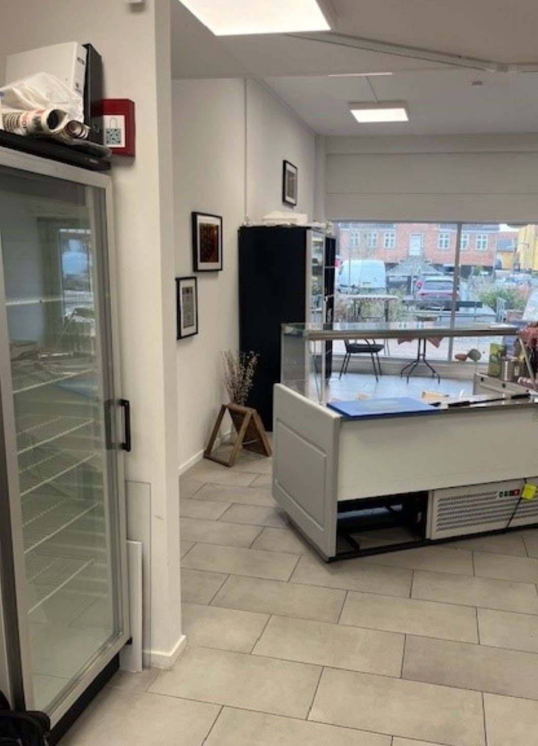 En glasdøret køleskab med en avis på toppen og en skrivebord med papir på den anden side af et glas vindue i en