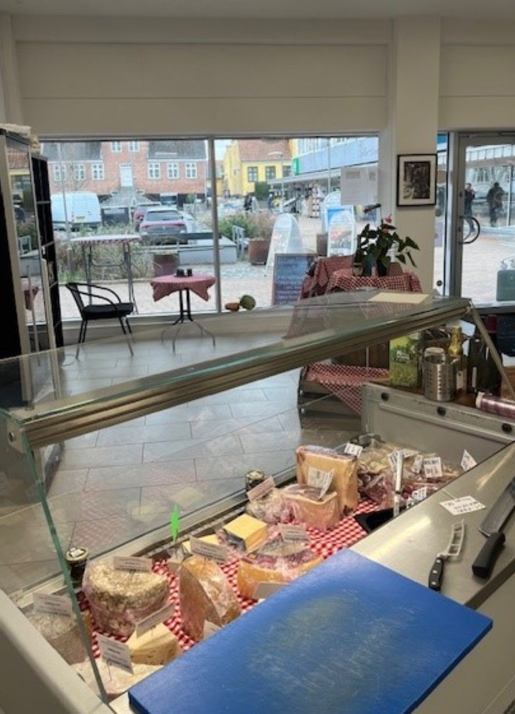 Køkken med glasbord og flere skiver ost og en kniv på skærebræt og flere ølflasker