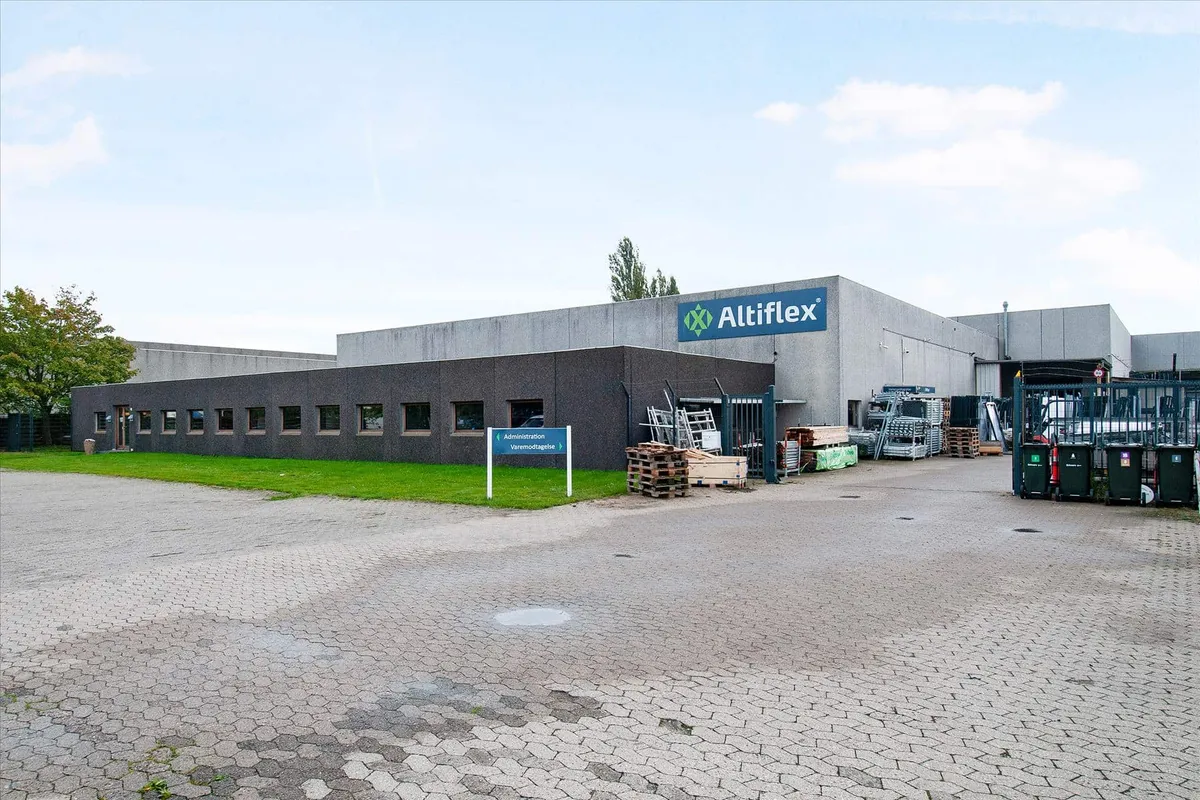 Kontorbygning med logoet Altiflex. En parkeringsplads med grønne søjler og to papirkurve. Administrationsskilt udenfor