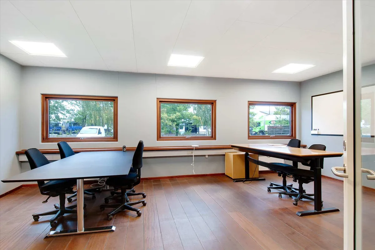 Et moderne mødelokale med to lange trægulve skriveborde, hver med fire stole og lys præsenterer et afslappet arbejdsområde