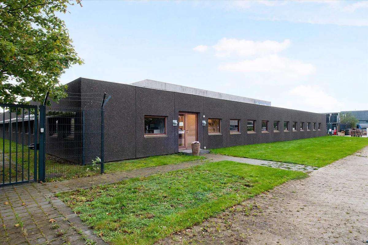 Moderne bygning med flere vinduer, parkeringsplads og grønne græsplæner uden for