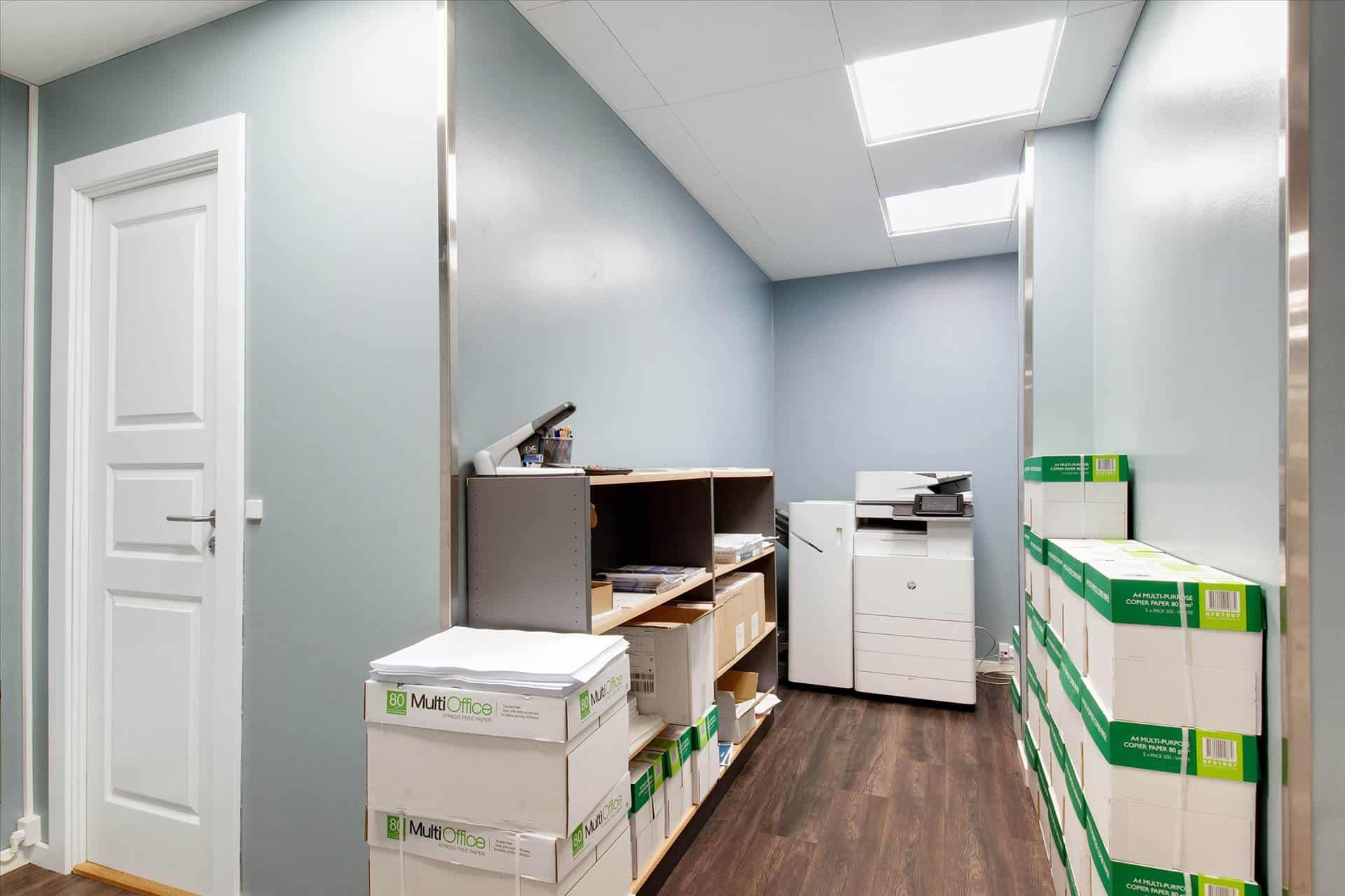 Kontorrum med mange papkasser og en printer, hvor der er høje lofter med hvide loftpaneler og lysekroner