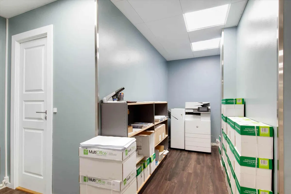 Kontorrum med mange papkasser og en printer, hvor der er høje lofter med hvide loftpaneler og lysekroner