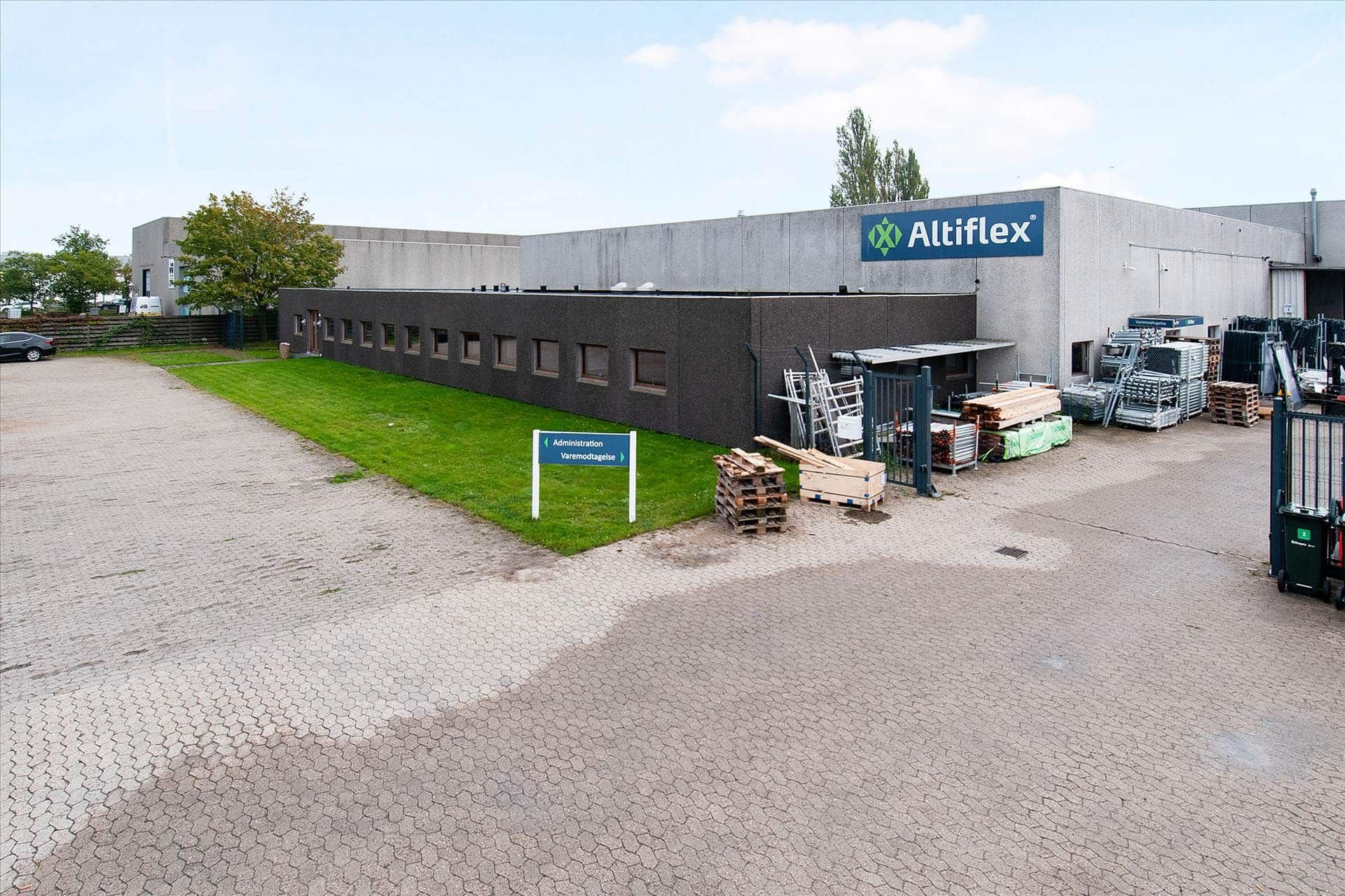 Et stort bygningskompleks med teksten Altiflex på siden og en græsplæne foran bygningen