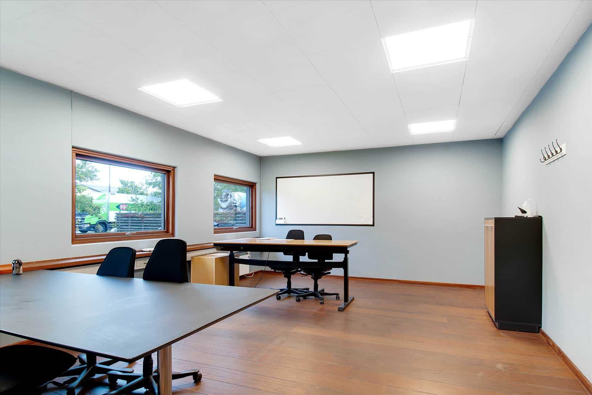 Store kontorrum med lyse lofter, lysegrå vægge og trægulve, to lange skriveborde og fem sæder samt et skrivebord med to