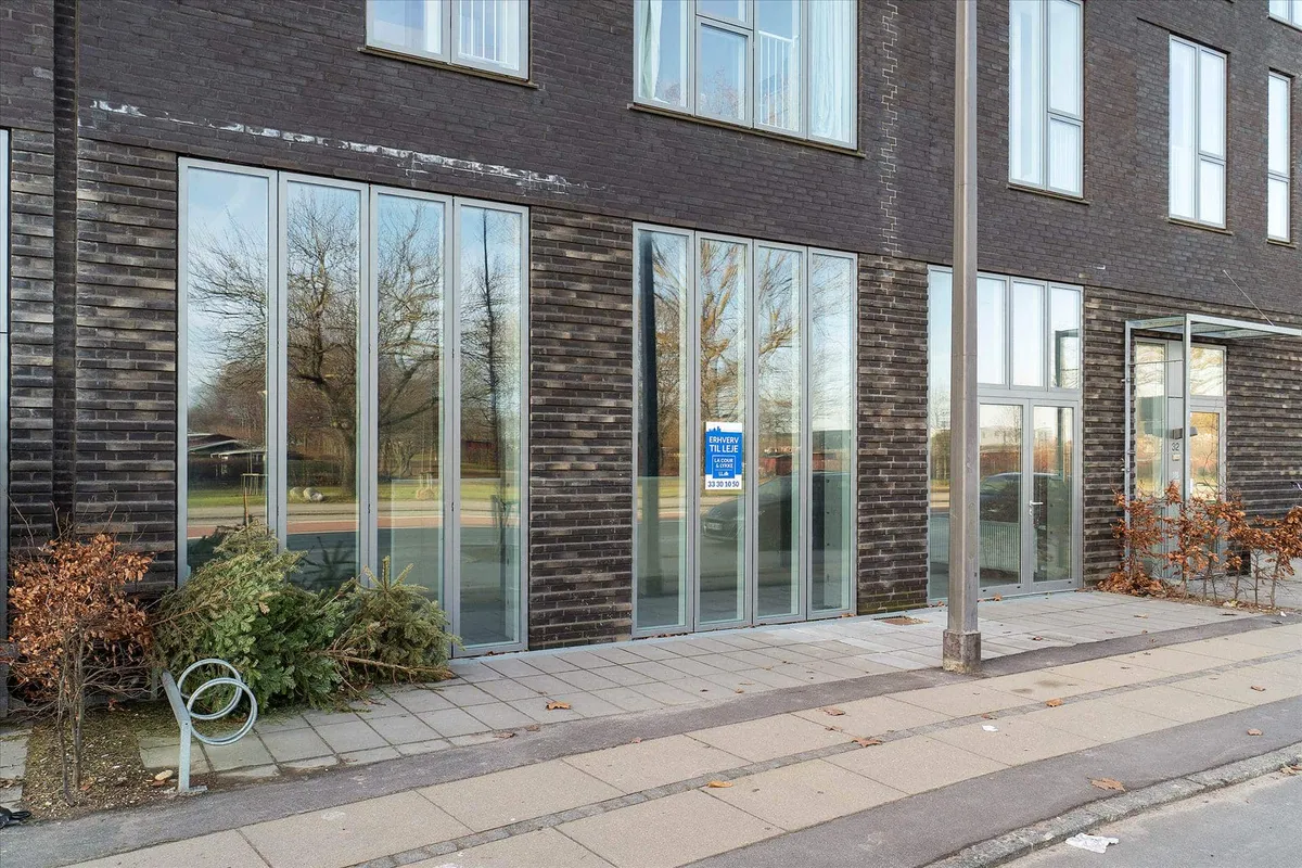 Moderne bygning med store glasruder og to indgange, hvor den ene er lukket med en blå skilt, som viser åbningstid.