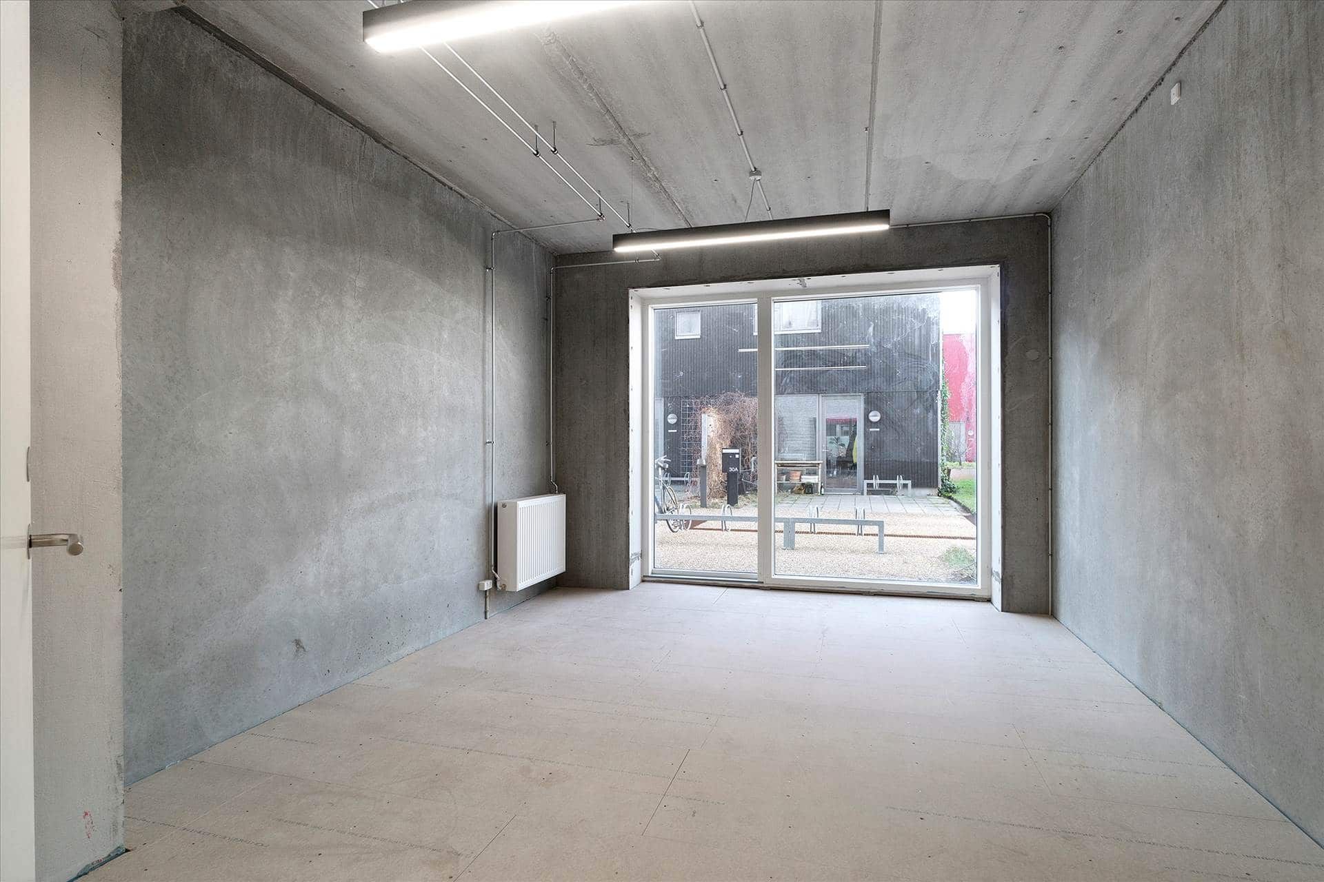 En stor, ubenyttet rum med hvide gulv, vægge og loft samt lyse glasdøre og en radiator på væggen