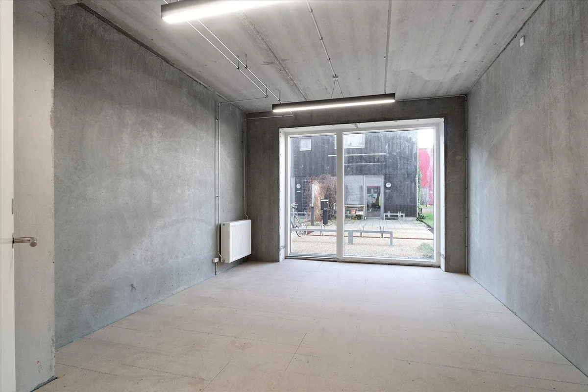 En stor, ubenyttet rum med hvide gulv, vægge og loft samt lyse glasdøre og en radiator på væggen