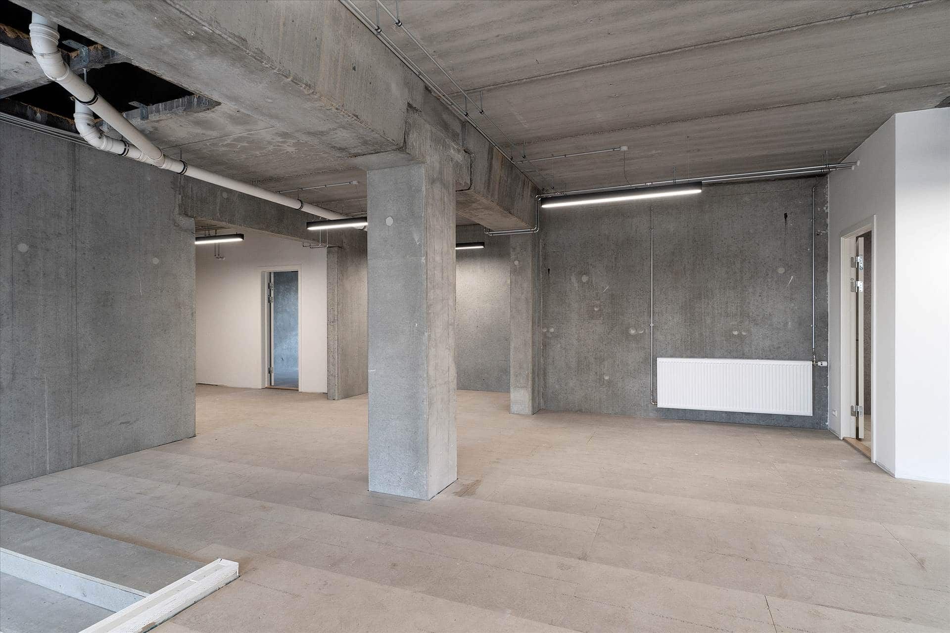 Rummelige erhvervslokaler med betonvægge, hvide lofter og åbne rum til indretning og møbler