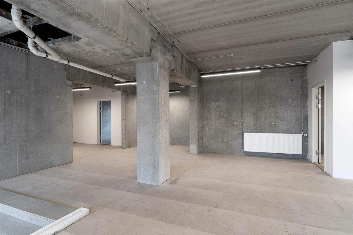 Rummelige erhvervslokaler med betonvægge, hvide lofter og åbne rum til indretning og møbler