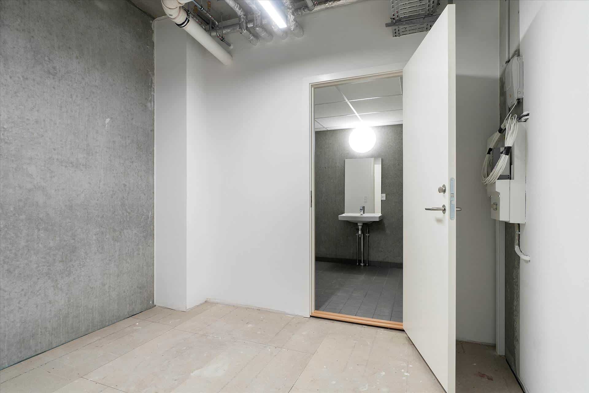 En ren vaskerum med hvide vægge, en åben dør, et spejl, en hvid vandhaner og en hvid håndvask