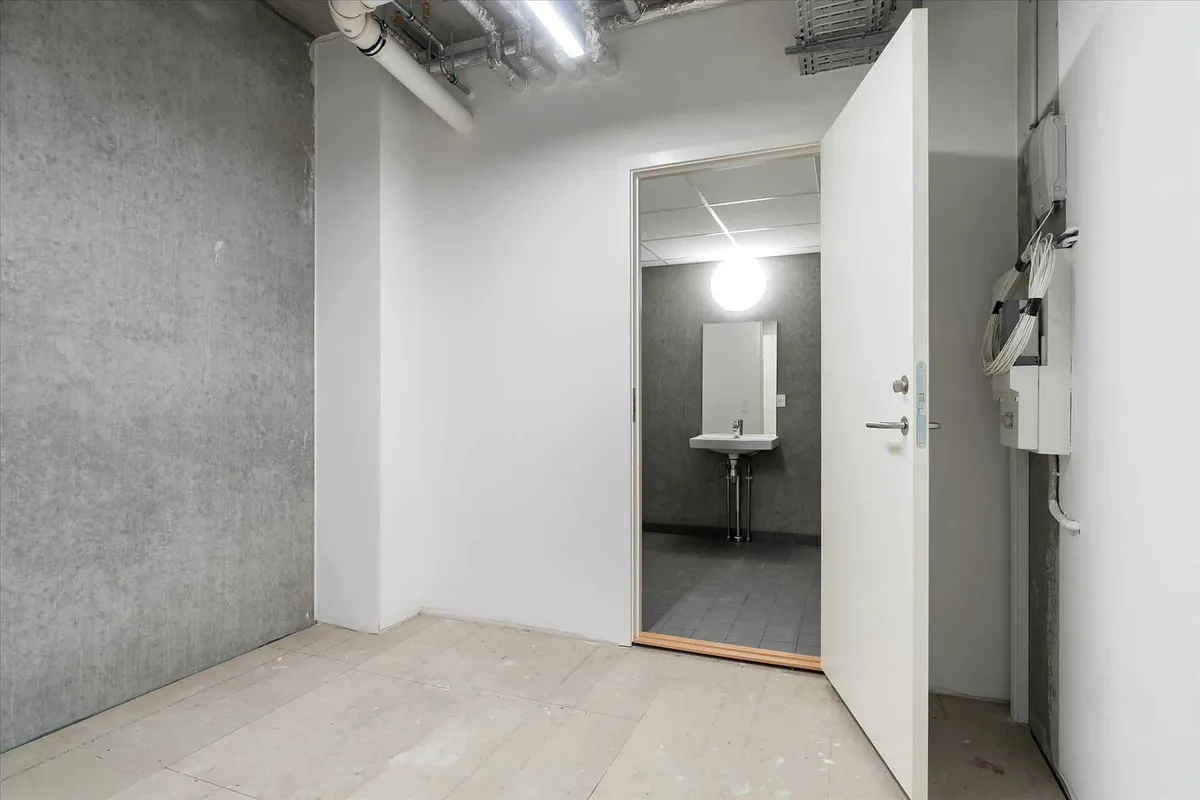 En ren vaskerum med hvide vægge, en åben dør, et spejl, en hvid vandhaner og en hvid håndvask