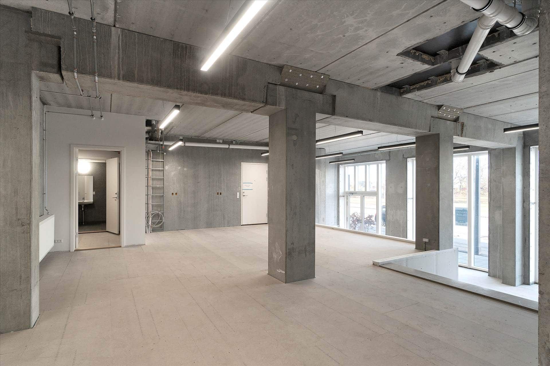En stor, åben erhvervslokal på Amager Strandvej med betongulv og vægge samt høje vinduer og indvendige søjler