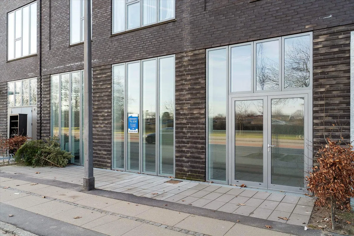 Glasdøre og vinduer med høj kvalitet ud til en vej med biler og træer, som udgør et moderne erhvervslokal på Amager Strandvej