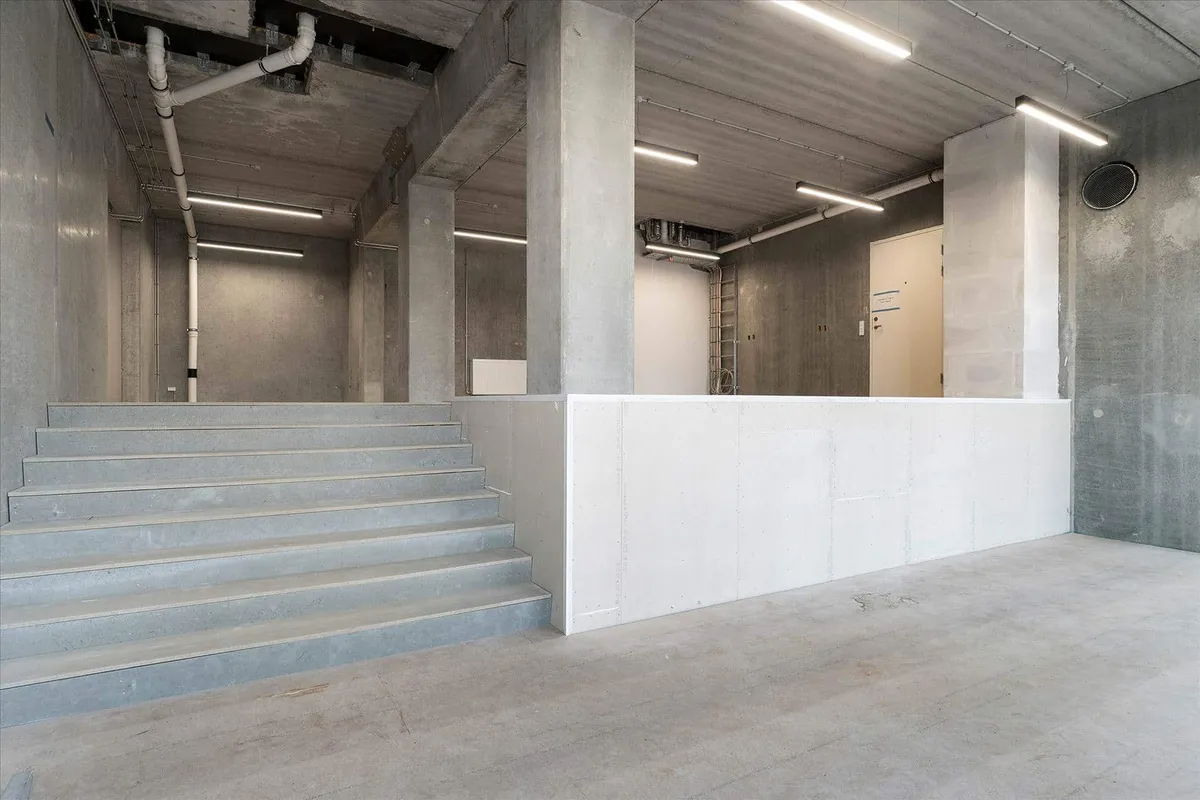 Betonvæggede lagerrum med åbne trapper og højloftede rum med lyse paneler, hvor der er adgang til en lukket dør og et åbent