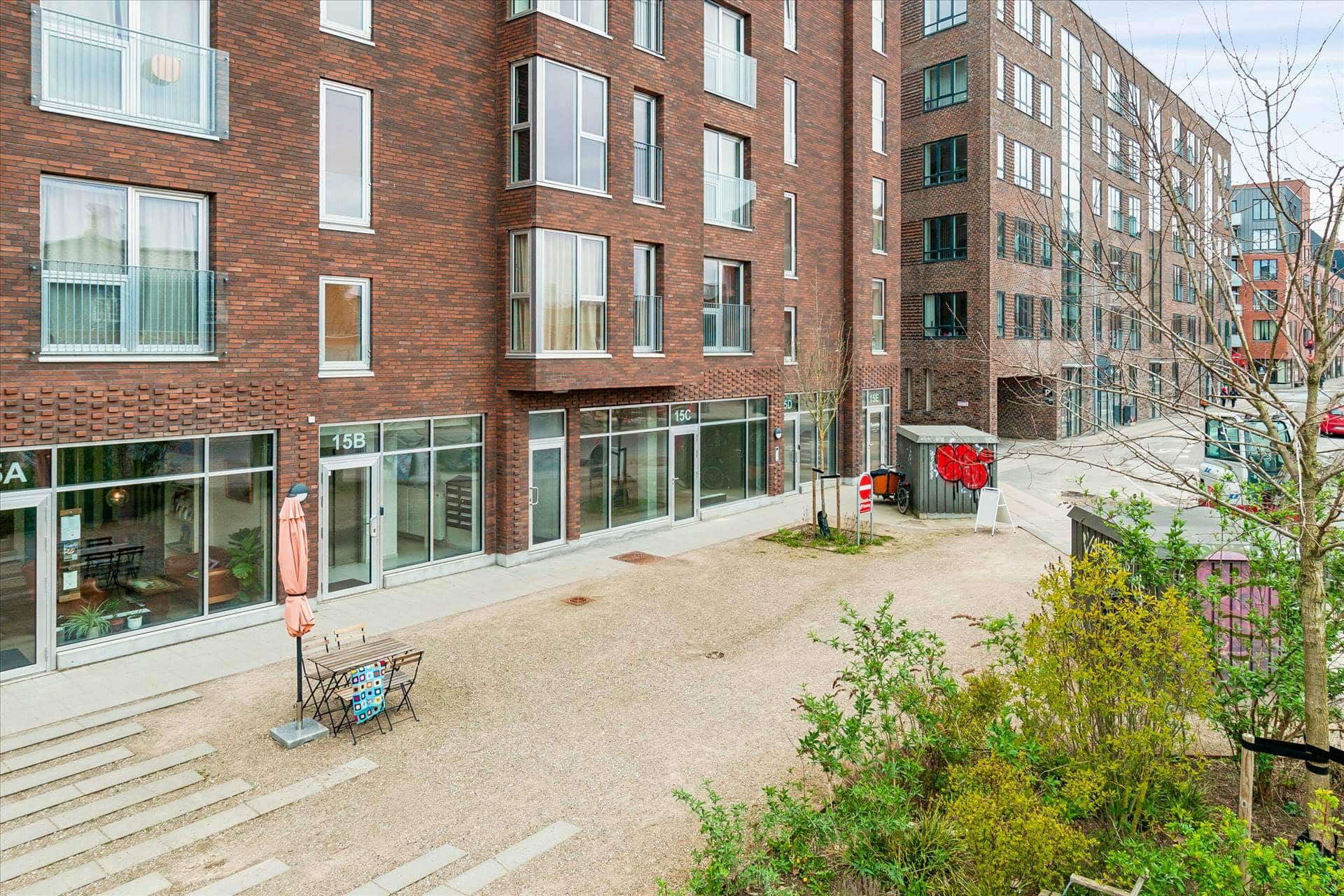 Moderne bygning med røde mursten, store glasruder, en åben dør og en terrasse med gult paraply i forgrunden