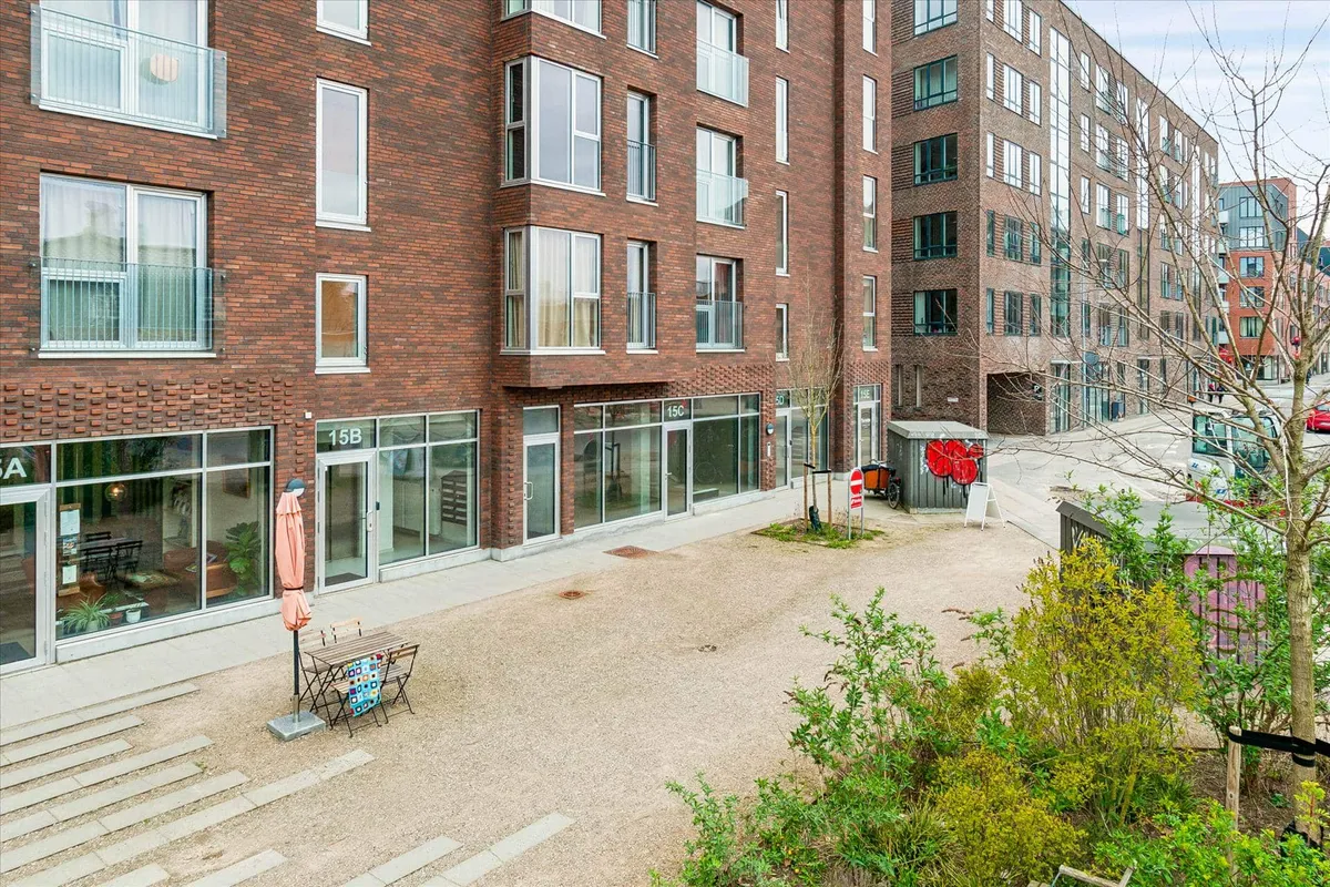 Moderne bygning med røde mursten, store glasruder, en åben dør og en terrasse med gult paraply i forgrunden