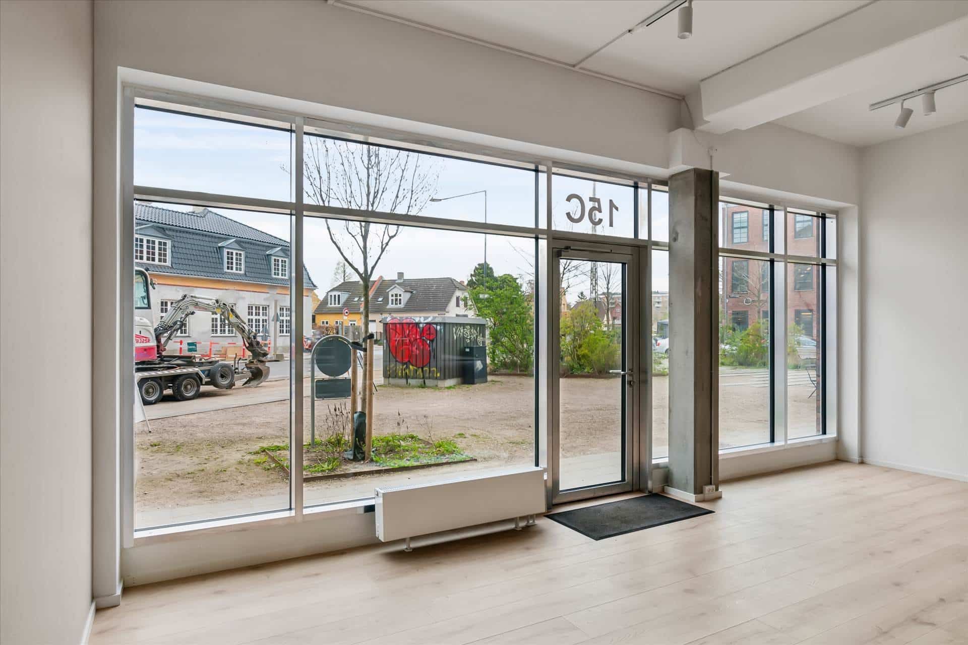 Showroom med store vinduer og højloft i Forfatterkvarteret, udvendigt med byggemaskiner og grønne buske