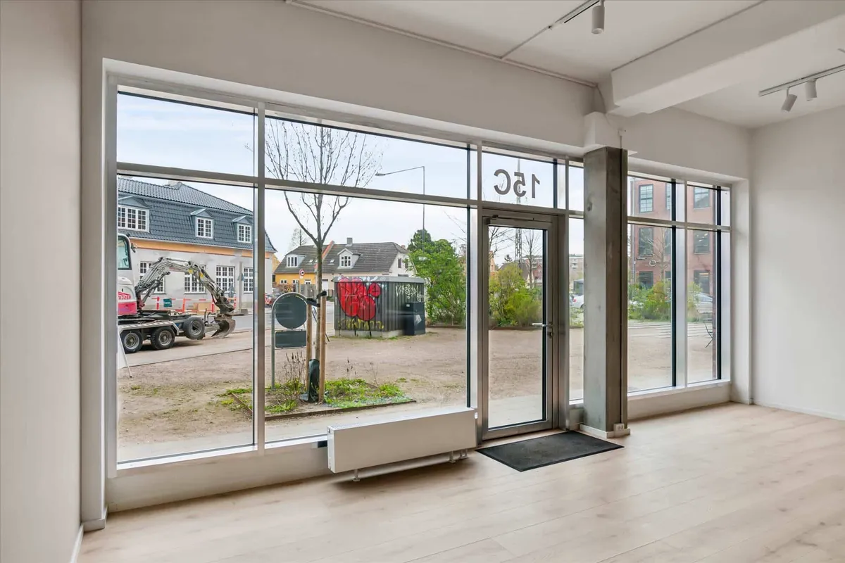 Showroom med store vinduer og højloft i Forfatterkvarteret, udvendigt med byggemaskiner og grønne buske