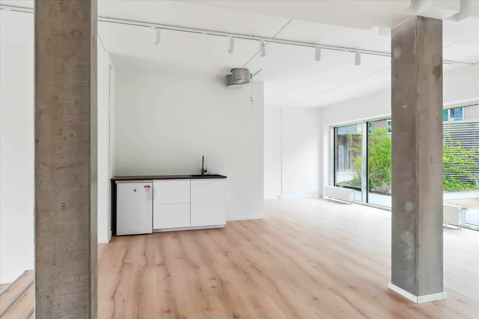 Tomt rum med hvide vægge og gulv samt et køkken med køleskab og håndvask