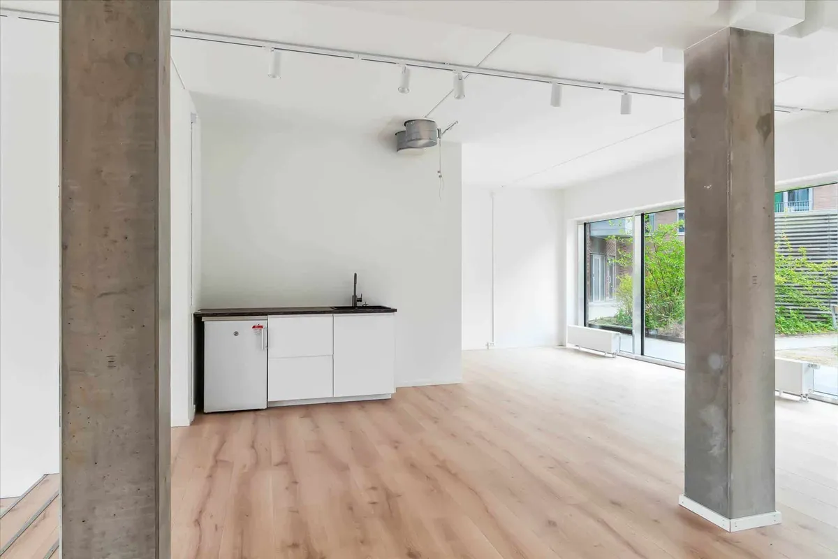 Tomt rum med hvide vægge og gulv samt et køkken med køleskab og håndvask