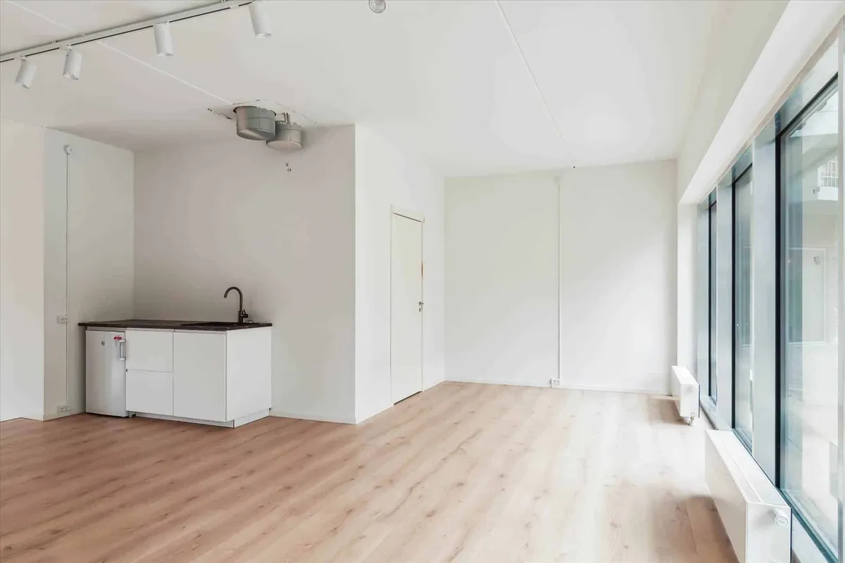 En tom køkkendeling med lyse hvide vægge, lyse trægulv og moderne køkkenudstyr med en vandhane og skarpe linjer på det hvide