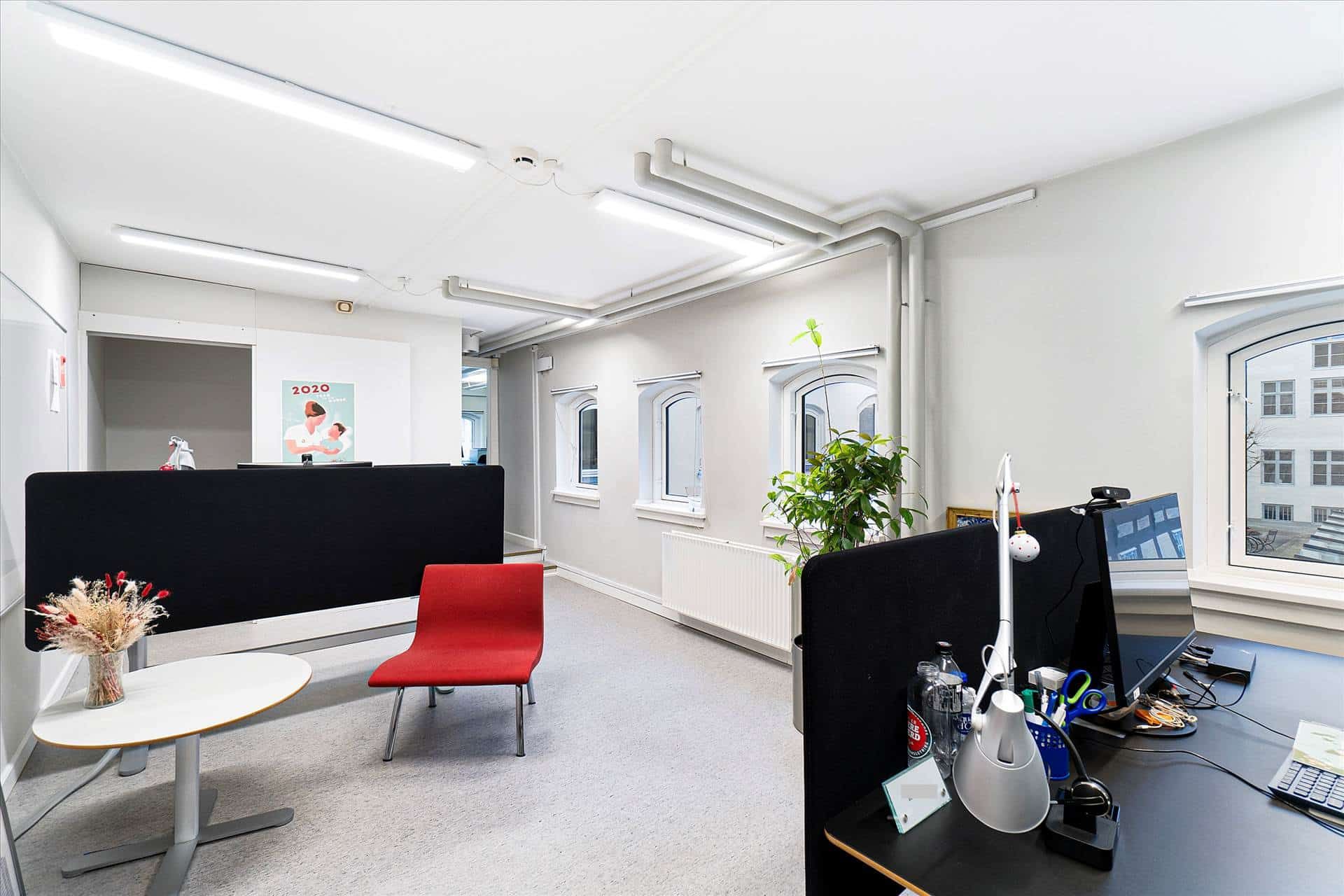 Udlejning af kontor i flot gårdhus, med skrivebord, bordlampe, vase med tørrede blomster og computer.