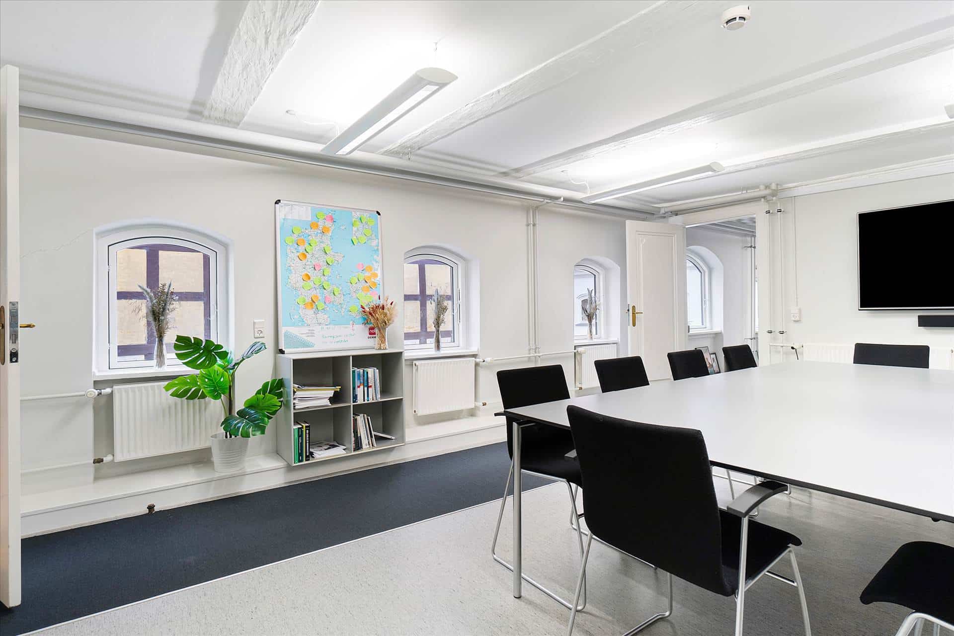 Det er et roligt kontor med hvide vægge, højt til loftet, lyse loftslamper, lysegulv og smukke gardiner ved de lyse vinduer