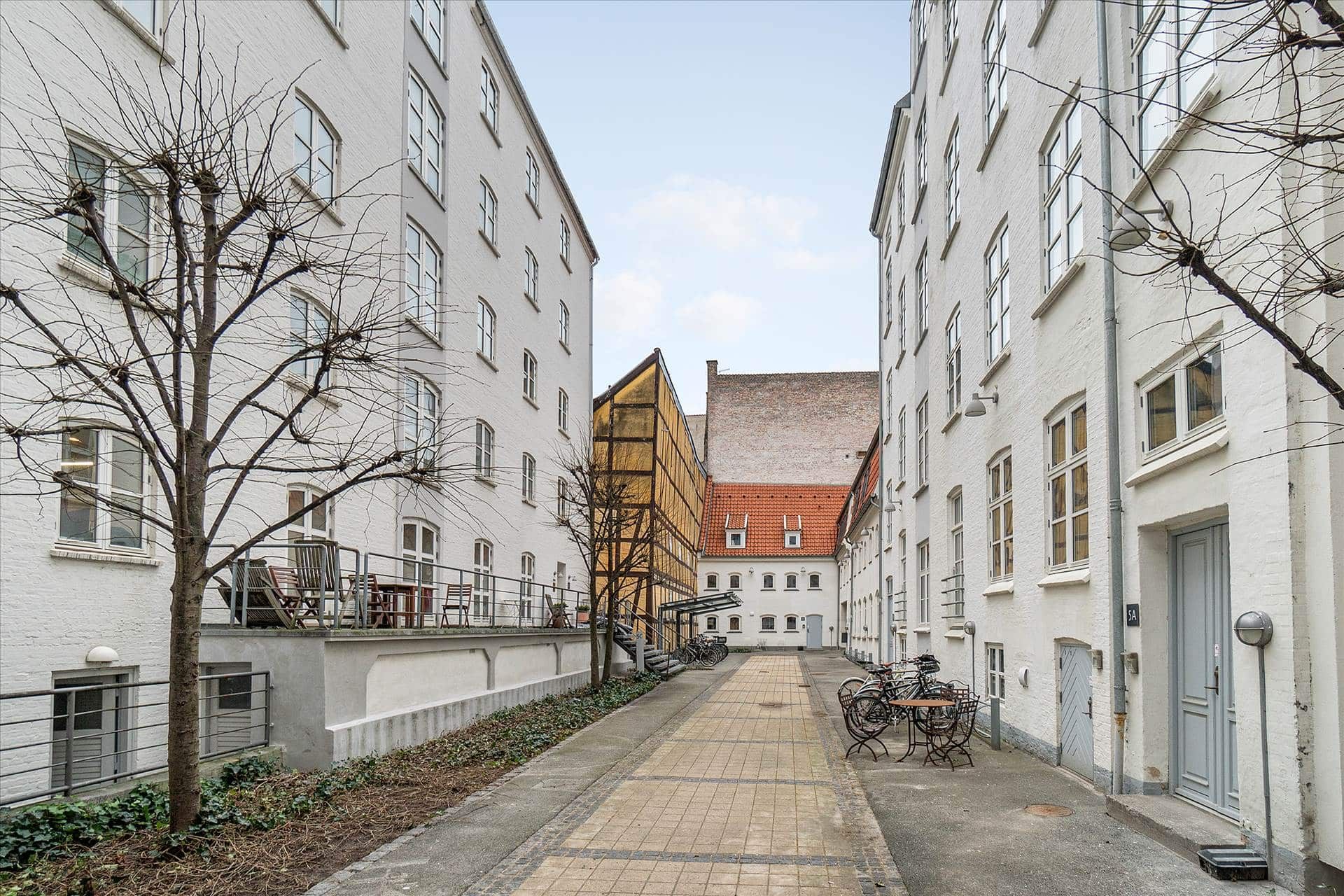 Det rolige gårdmiljø med lyse husstande, smukke træer og søjler, der afgrænser gangvejen mellem bygningerne