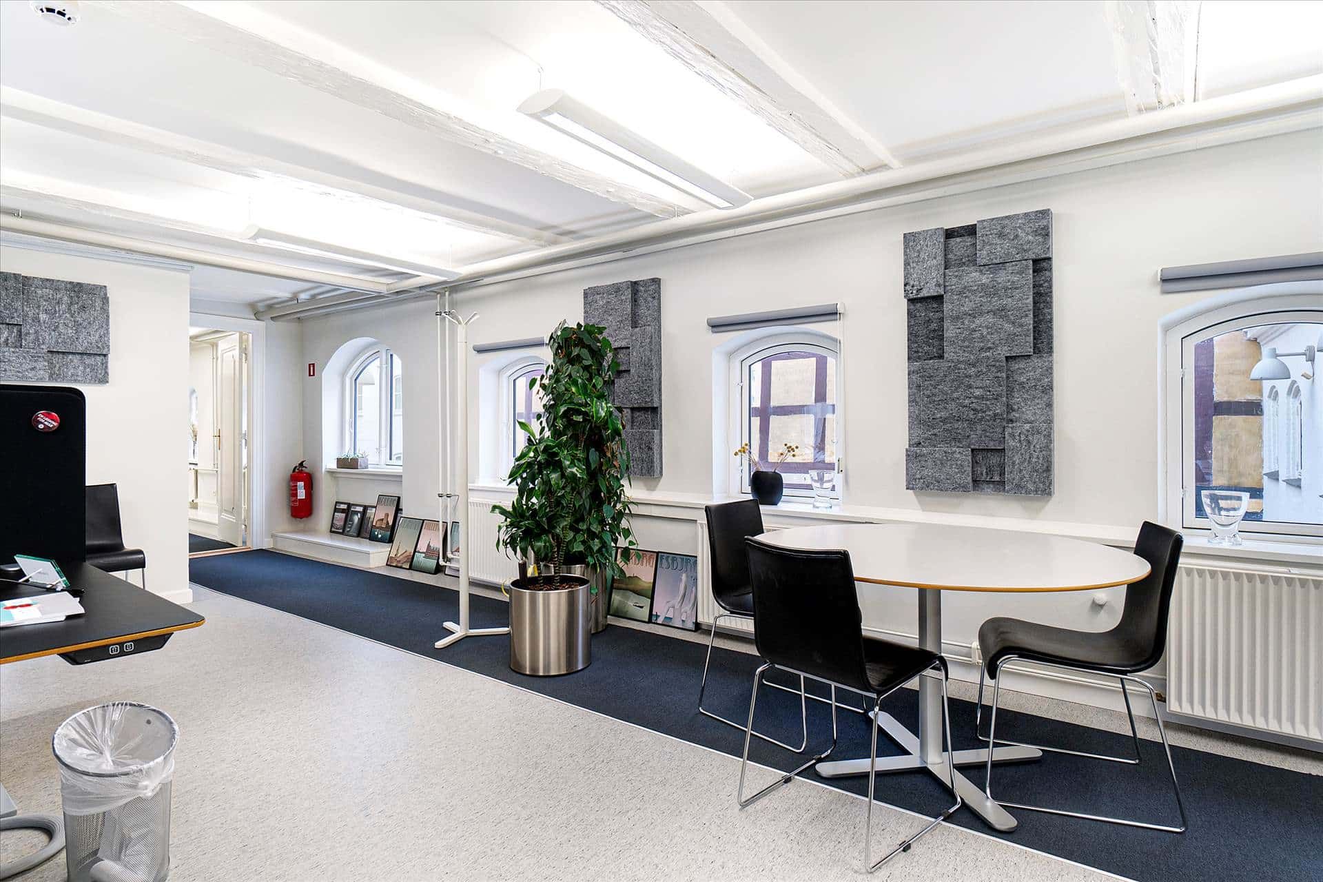 Kontor med lyse, lysegule vægge, hvide lofter, runde bord, læderstole og plante i en stålpotte.