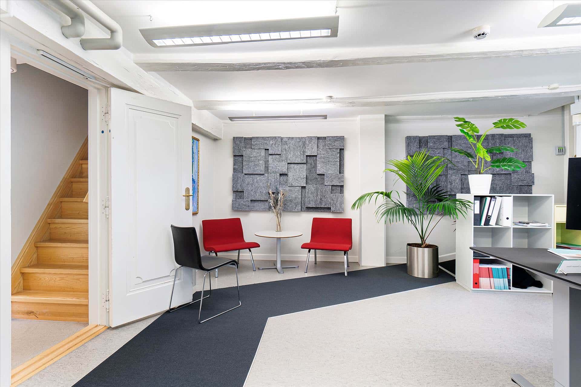 Moderne kontor med højt til loftet og en stor plante. To røde stole og en hvid stol er placeret ved væggen. Et bord og en