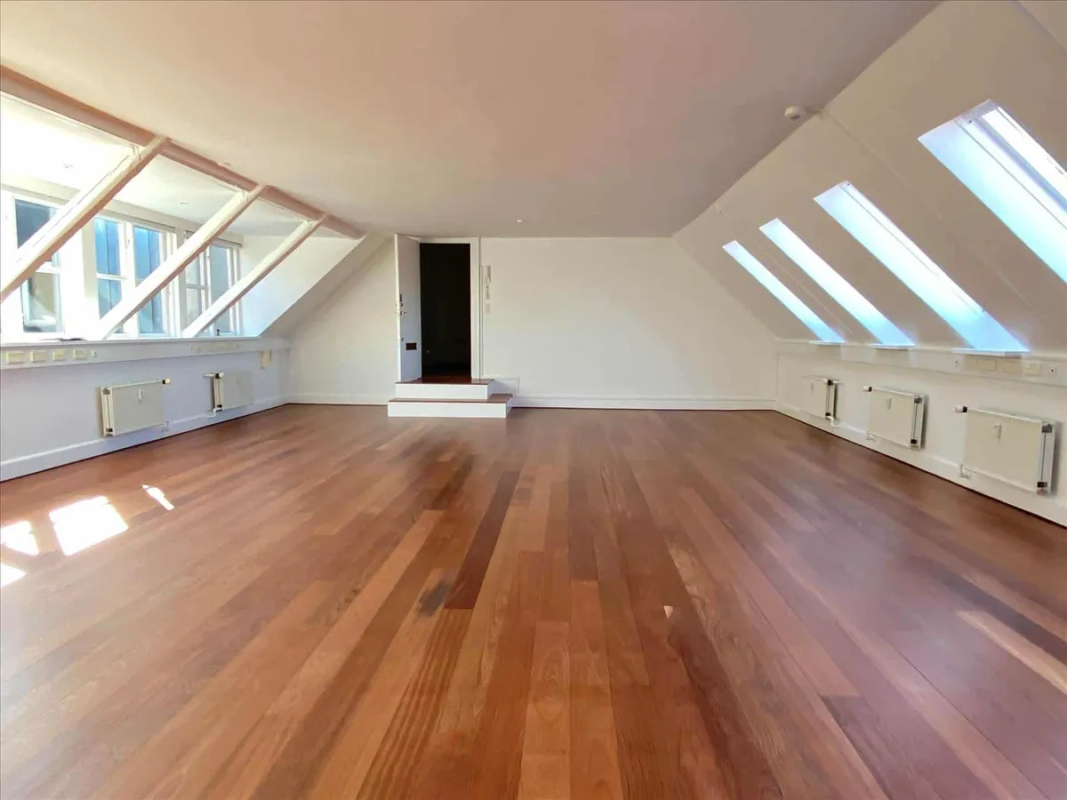 Nyrenoveret storrumskontor med trægulv og højloft. Hvide vægge og lofter med mange vinduer og loftsvinduer. Et trappeforløb