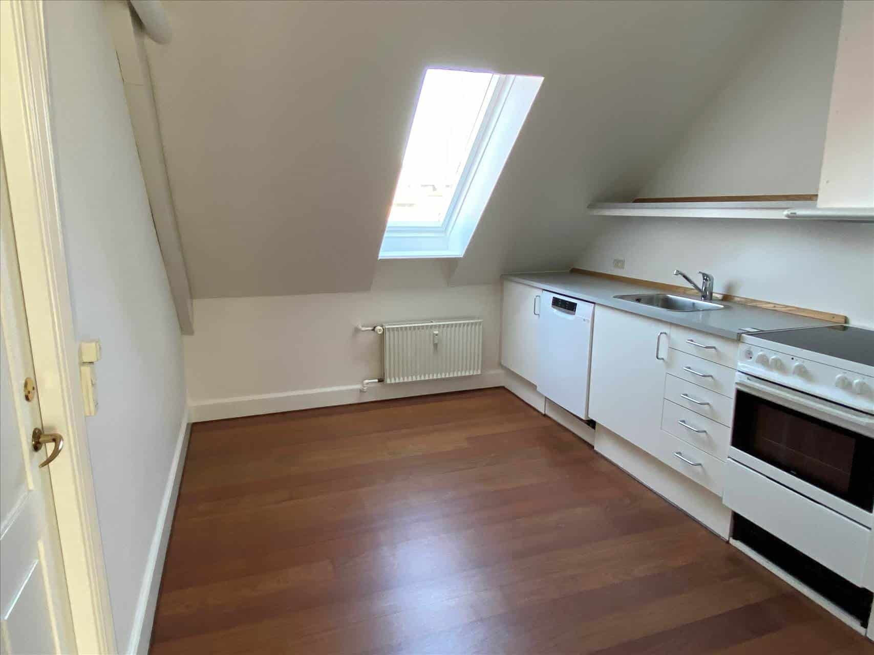 Et lyst og nyt loftsrum med højloft og et vindue med udsigt til byens tage. Et komplet køkken med en ovn, komfur,