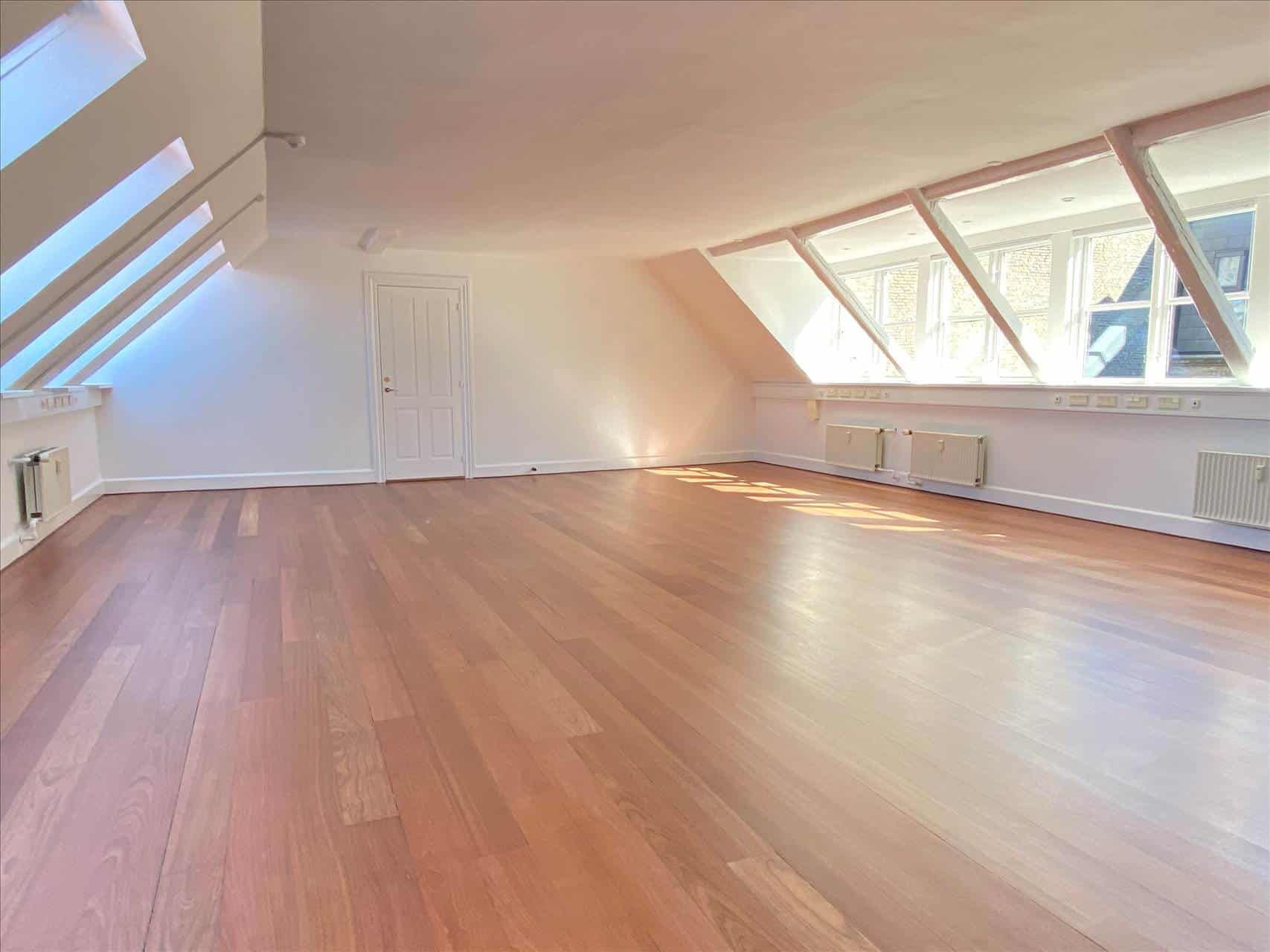 Storrumskontor med massivt trægulv og hvide vægge samt lyse loftsvinduer og højt til loftet