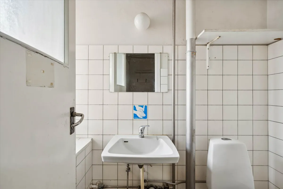 Hvidt toilet med håndvask og spejl samt urinal. Alle dele er malet hvidt og er i god stand