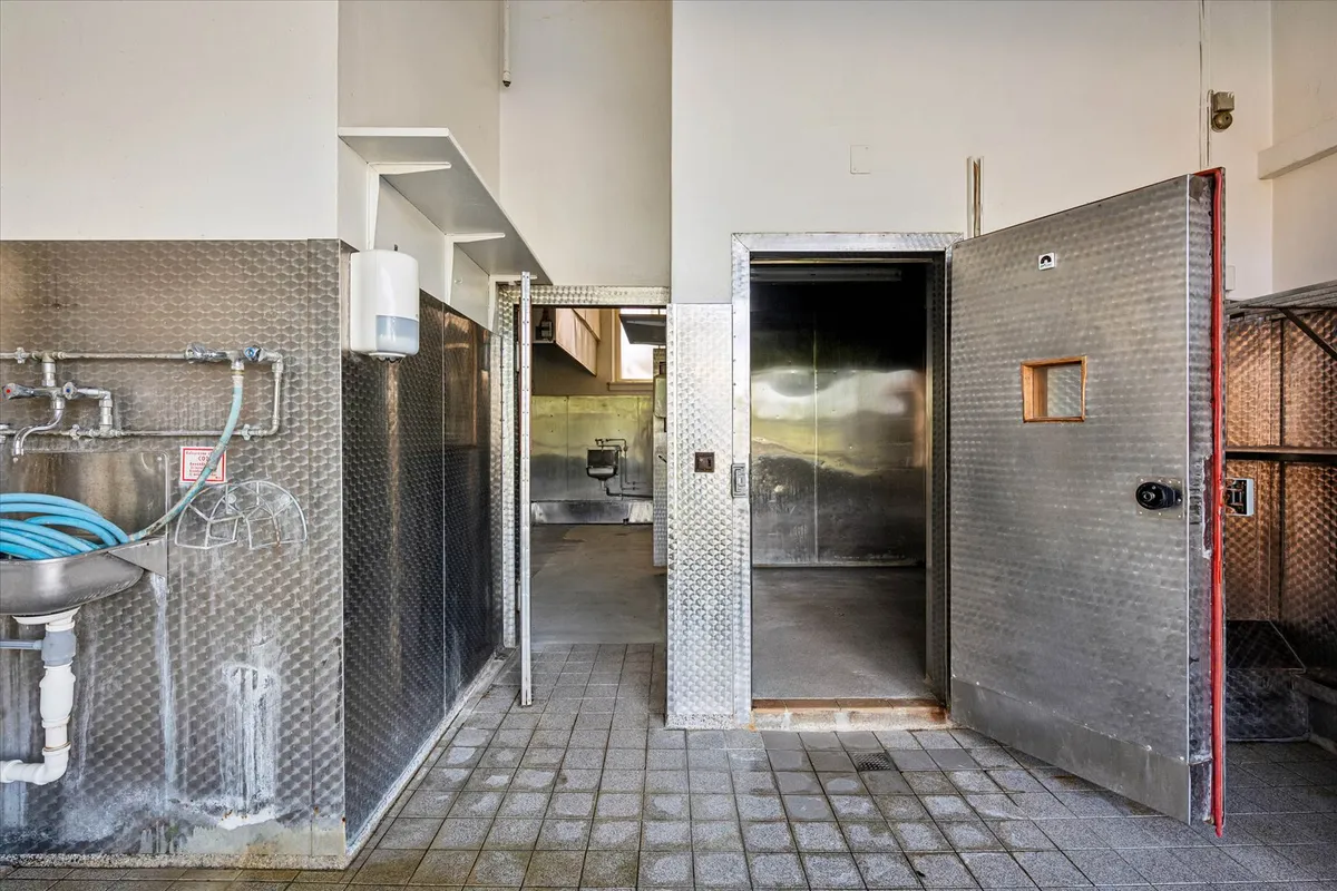 En lukket lagerdør med et lille vindue og en åben dør i en stor hall med en vaskebækken og et toilet.